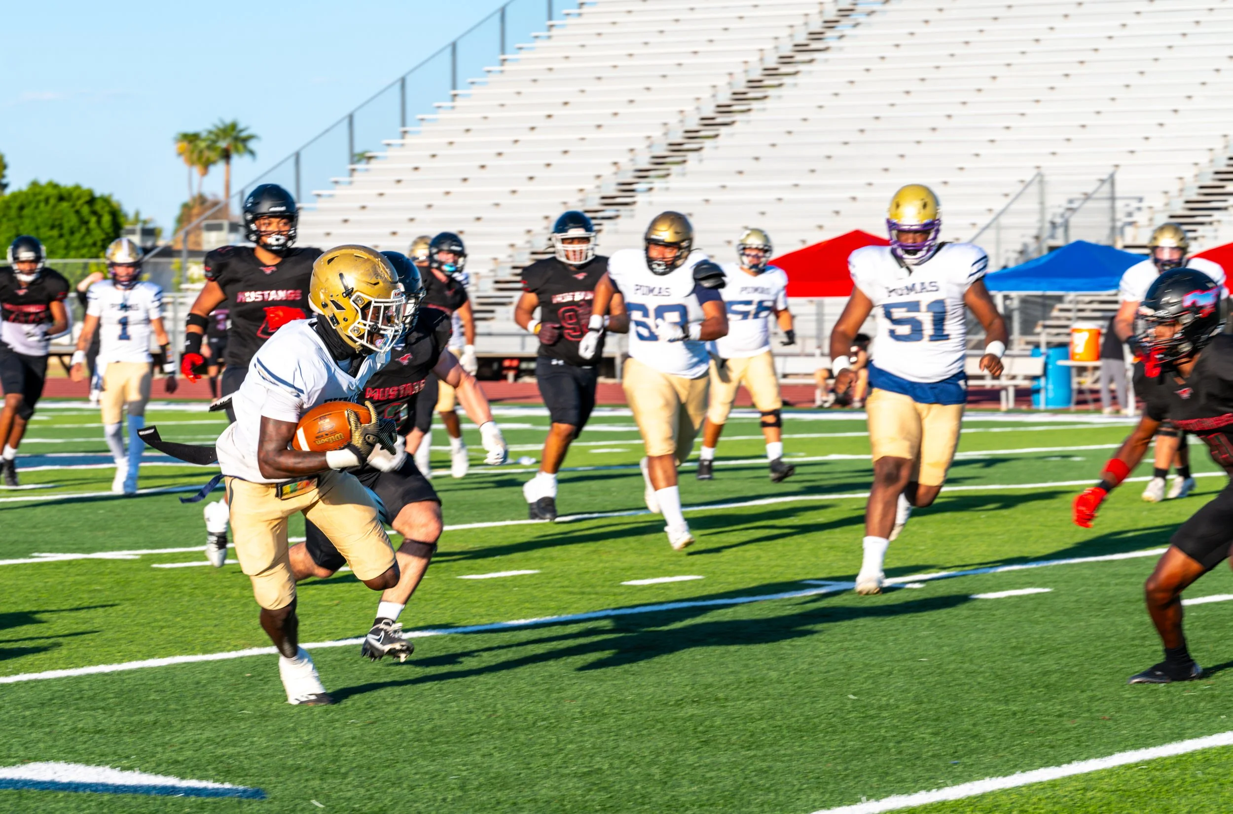 American football players in black, white, and gold uniforms on a field during a game, some running with the ball and others defending or observing.