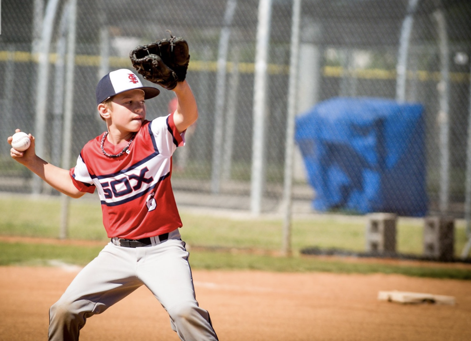 Young boy playing baseball, preparing to throw a ball while wearing a red and white baseball uniform and glove on a baseball field.