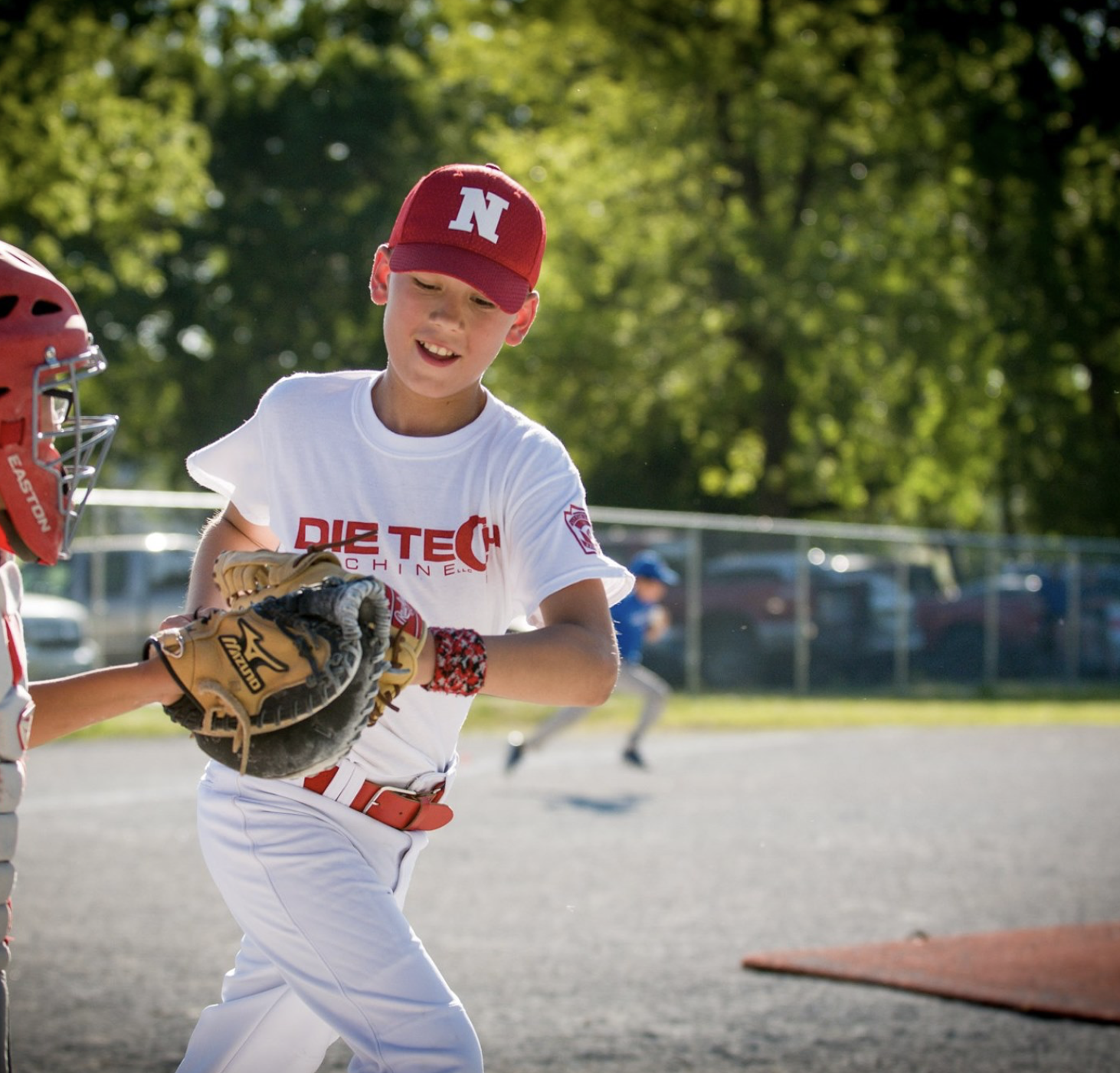 Young boy in a red cap and white baseball uniform playing baseball with a glove, on a sunny field.