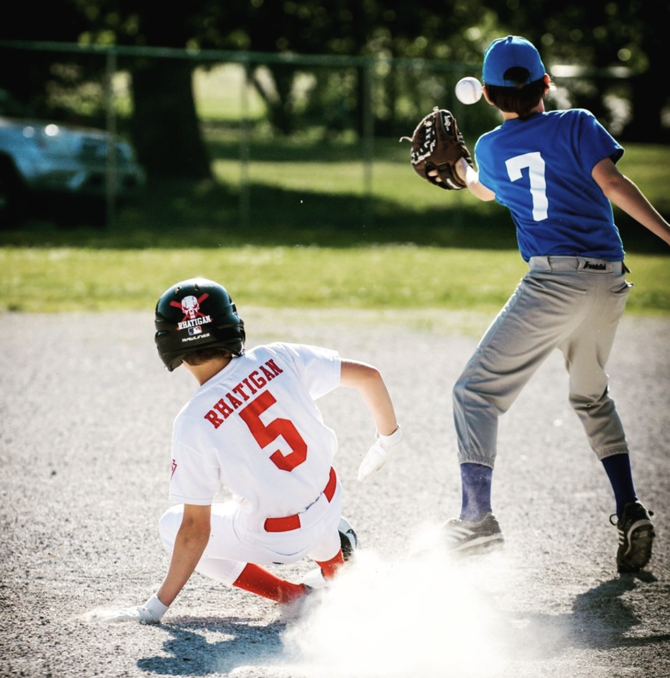 Two young boys playing baseball on a dirt field, with one sliding into a base while the other prepares to catch the ball.