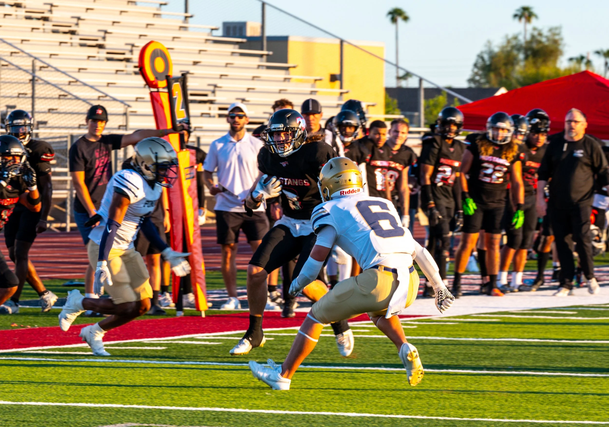 American football game with players in black and white uniforms on the field, one player running with the ball, and other players, coaches, and spectators watching.