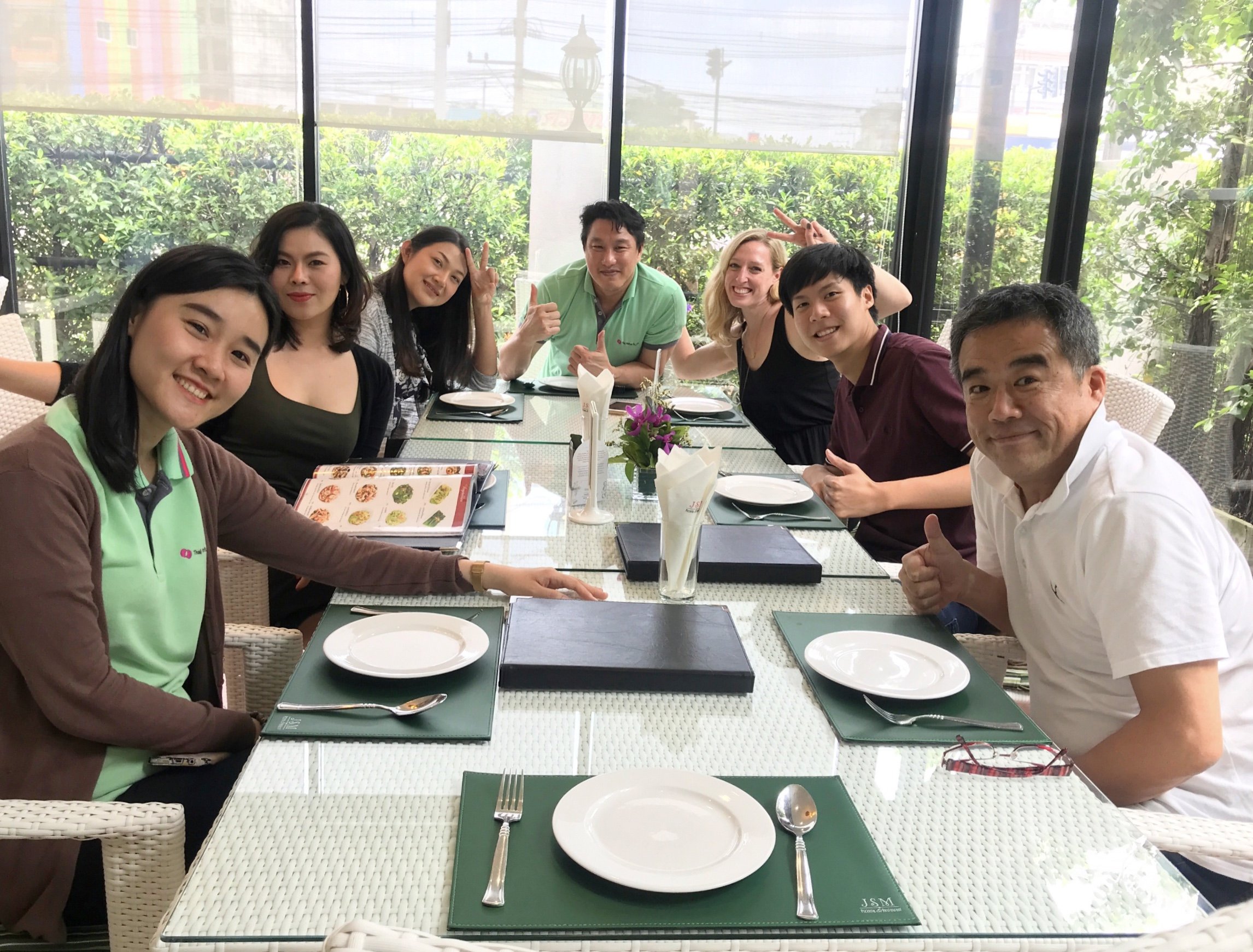 Group of people sitting at a dining table with empty plates and menus, smiling and posing for a photo indoors.