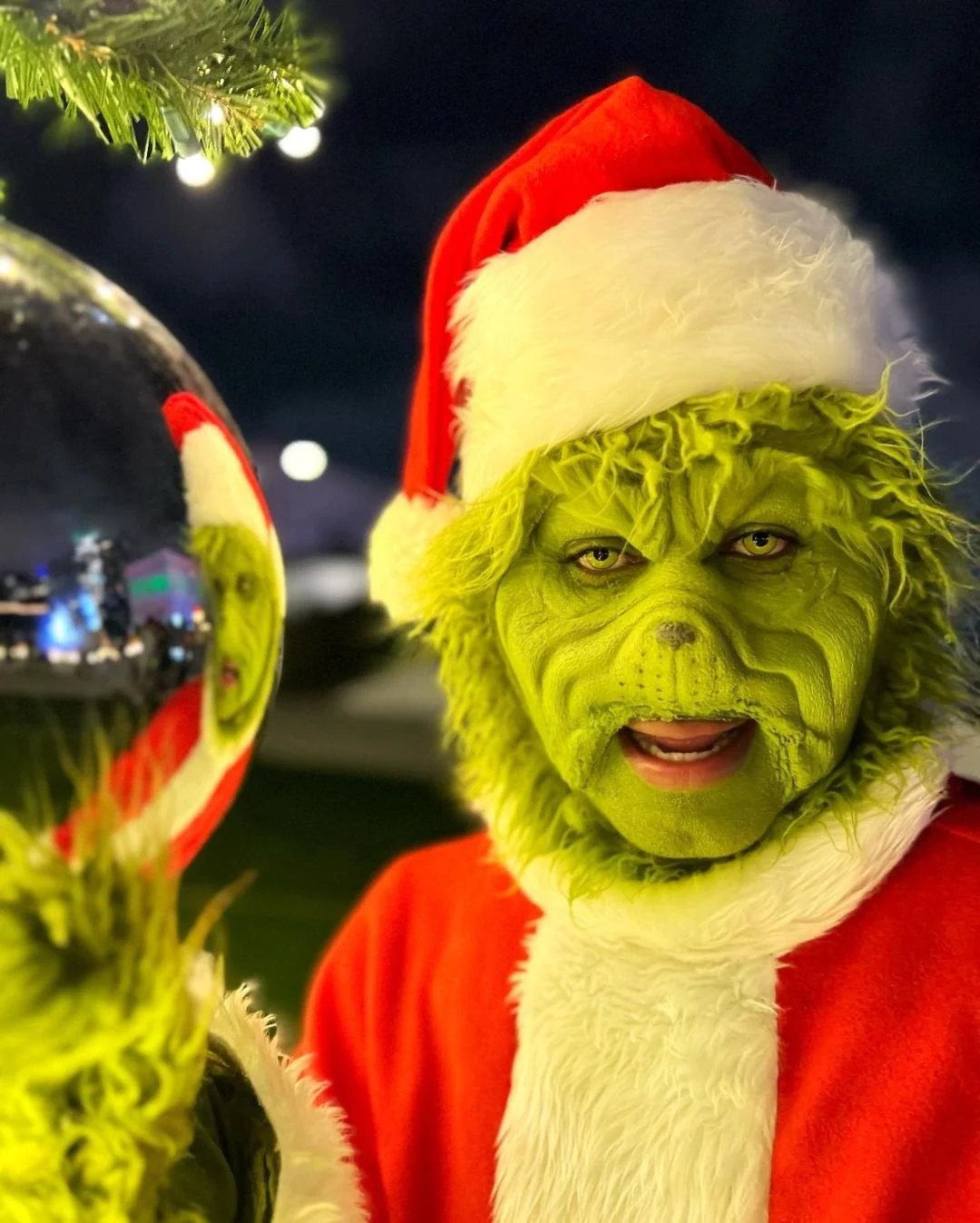 The Grinch dressed as Santa Claus holding a Christmas ornament.