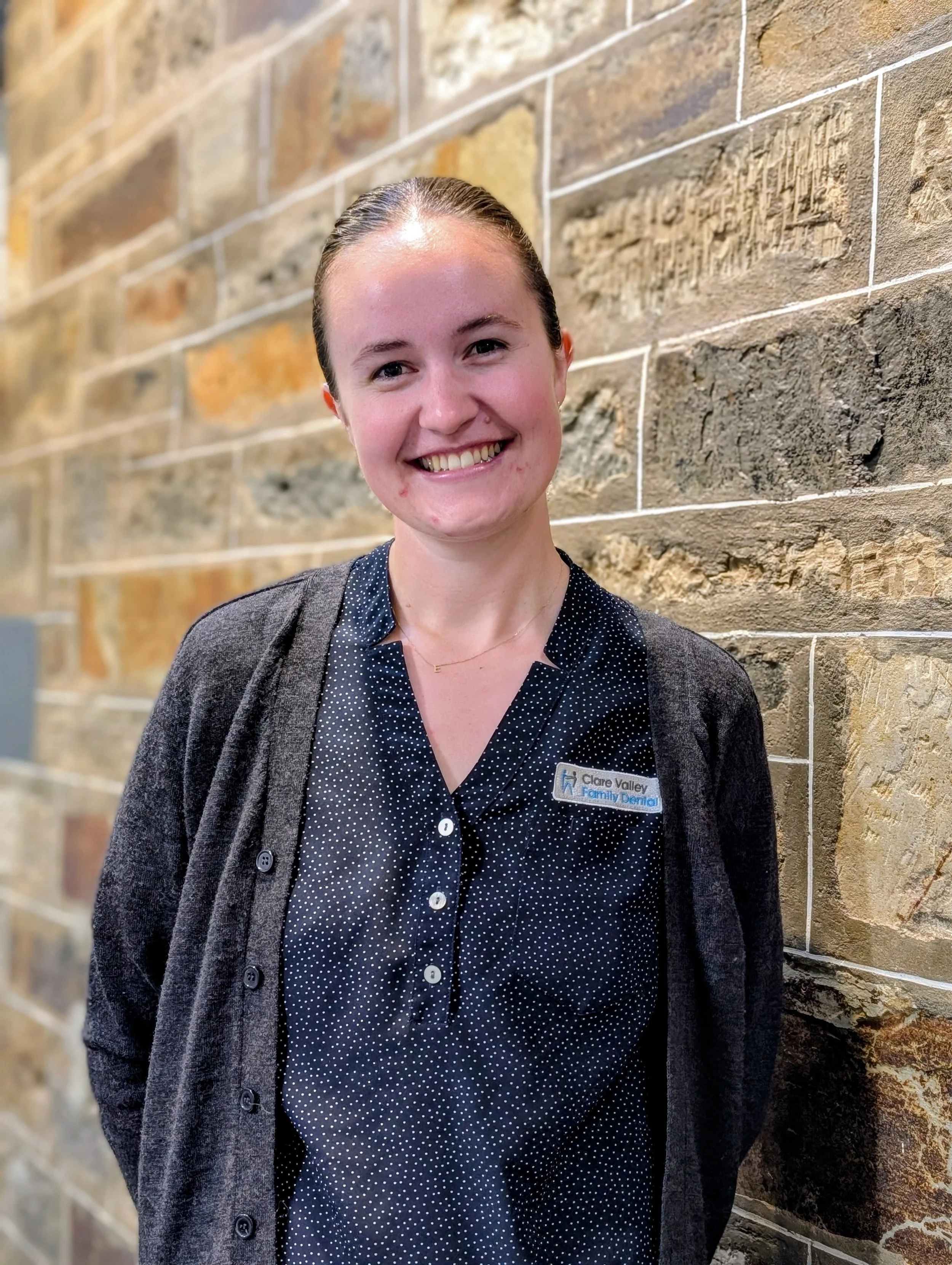 Portrait of a smiling woman in a blue uniform standing against a brick wall.