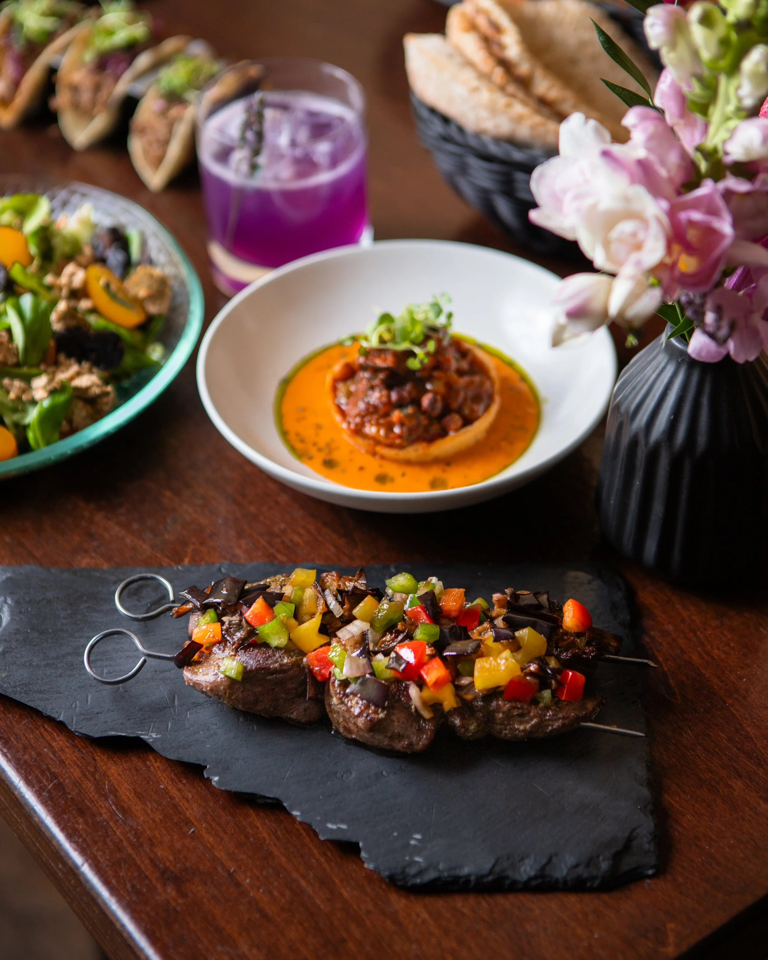 Levantinische Gerichte zum Teilen, Kebab-Spieße und ein Cocktail auf einem Tisch im „963 Berlin“