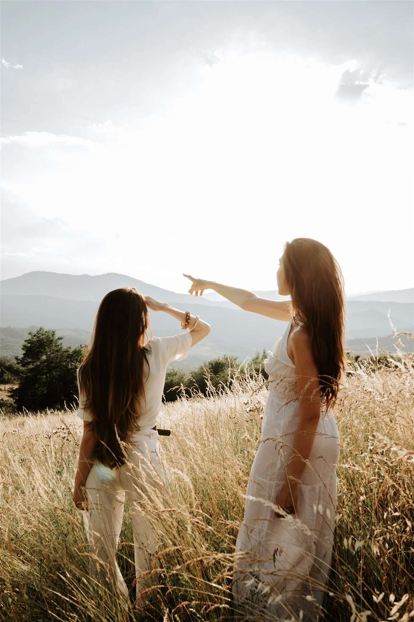 Due amiche di spalle in un campo in Toscana, una indica il sole: shooting di Matilde Rindi, fotografa a Prato