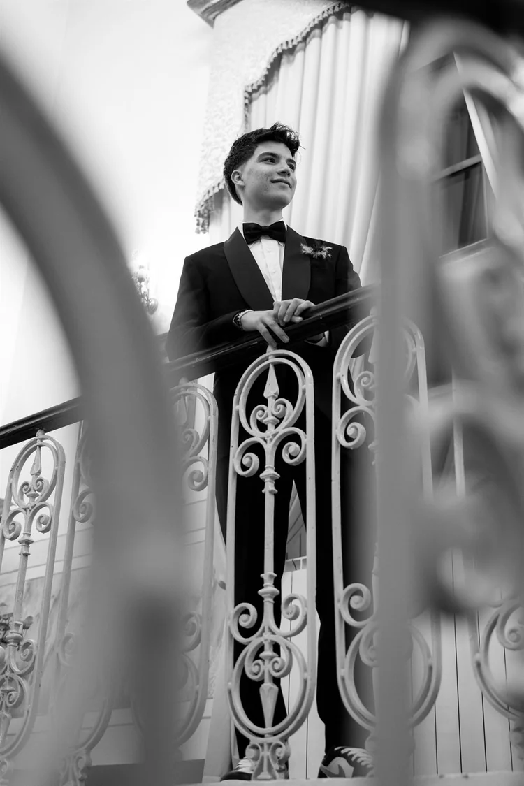 Festa in bianco e nero: ragazzo in smoking su un balcone in ferro battuto, foto di Matilde Rindi, fotografa a Prato