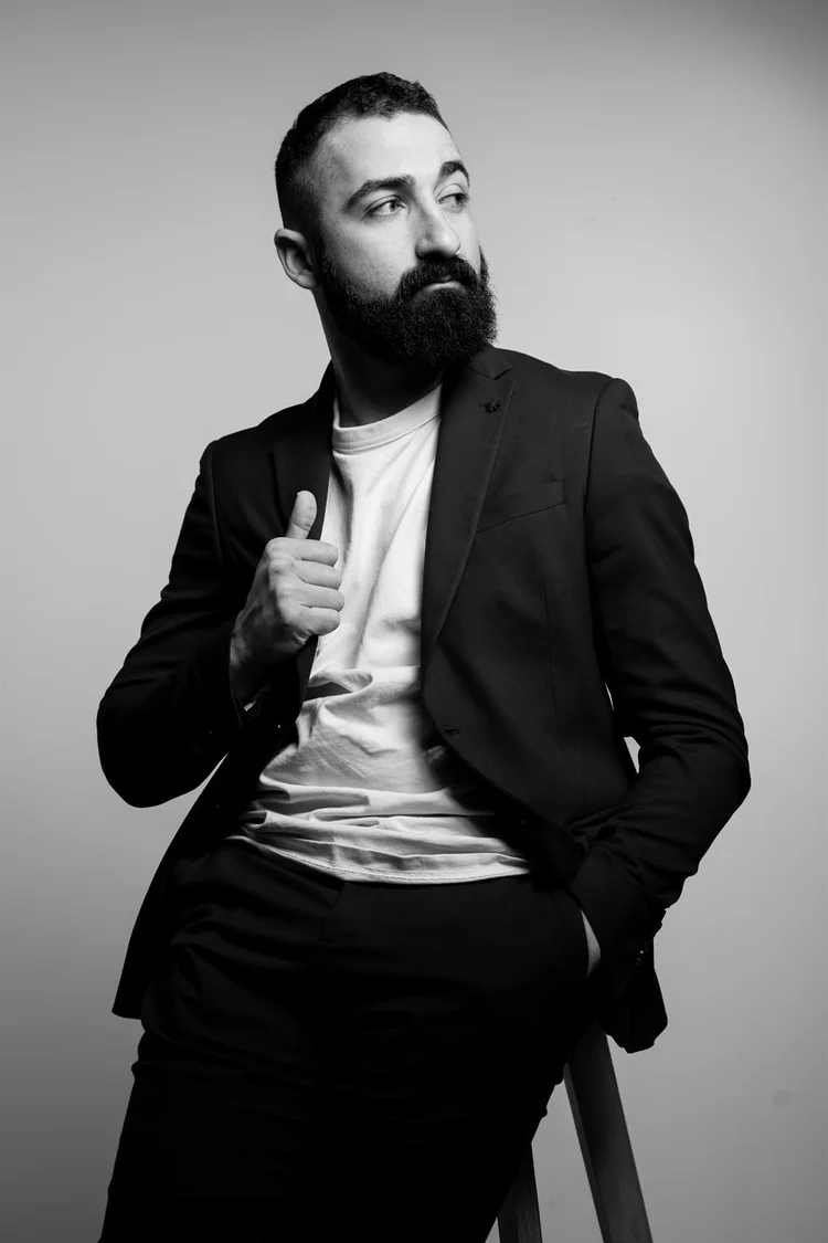 Book attore in bianco e nero con giacca scura, seduto su uno sgabello, foto di Matilde Rindi, fotografa a Prato