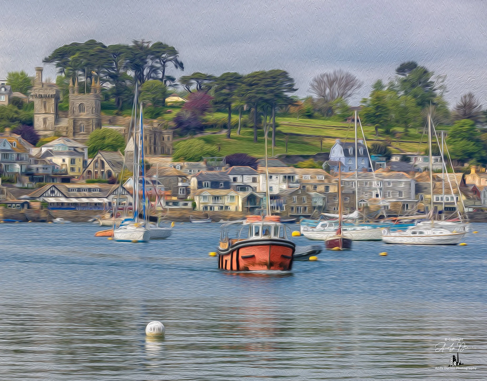 The Polruan ferry crossing the River Fowey.  A harbour scene with sailboats and a red boat in the water, houses on the shoreline, a green hillside with trees in the background, and a cloudy sky.