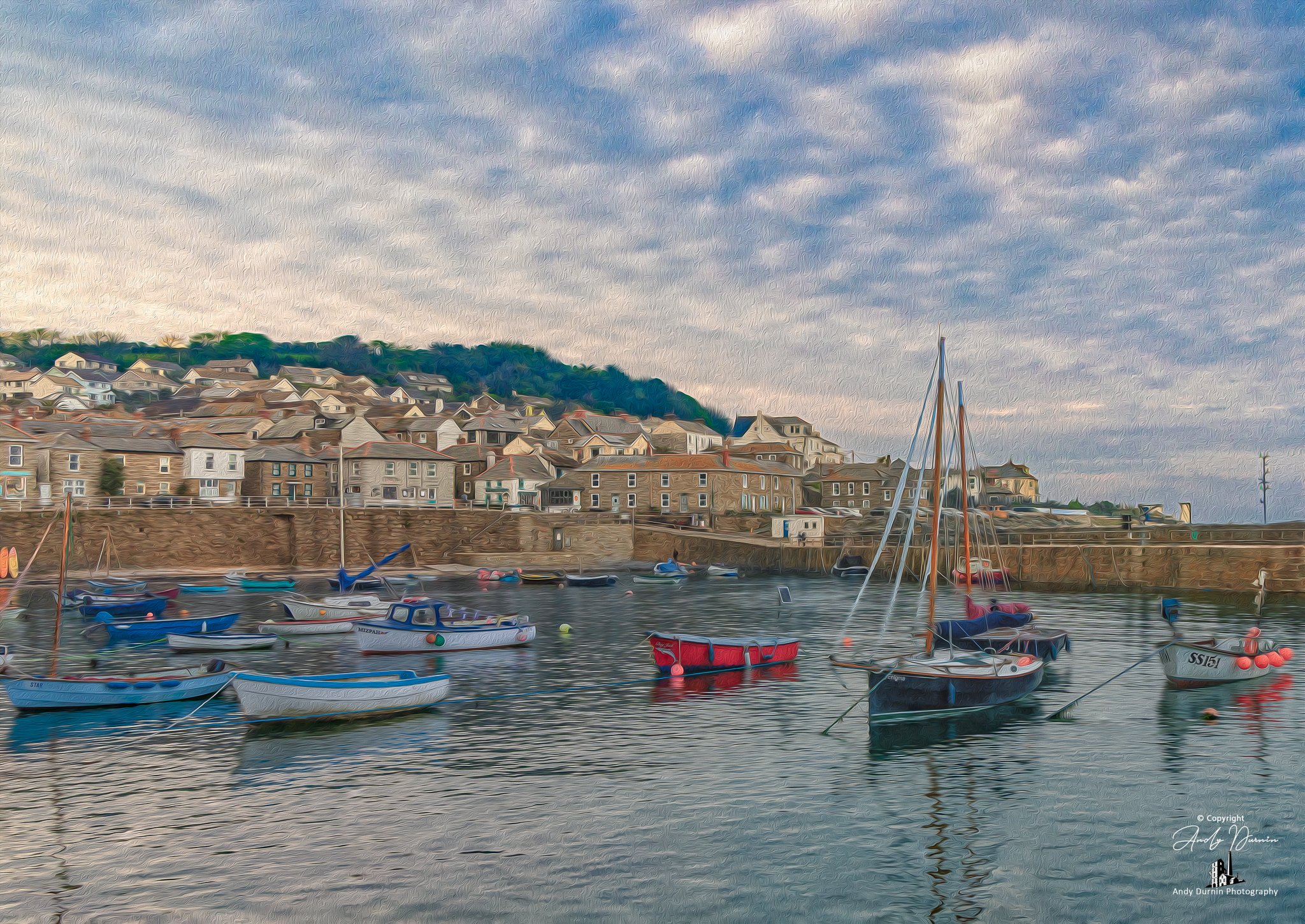 Mousehole Harbour, Cornwall A harbour with several small boats and sailboats floating on calm water, with a background of a hillside densely packed with houses under a partly cloudy sky.