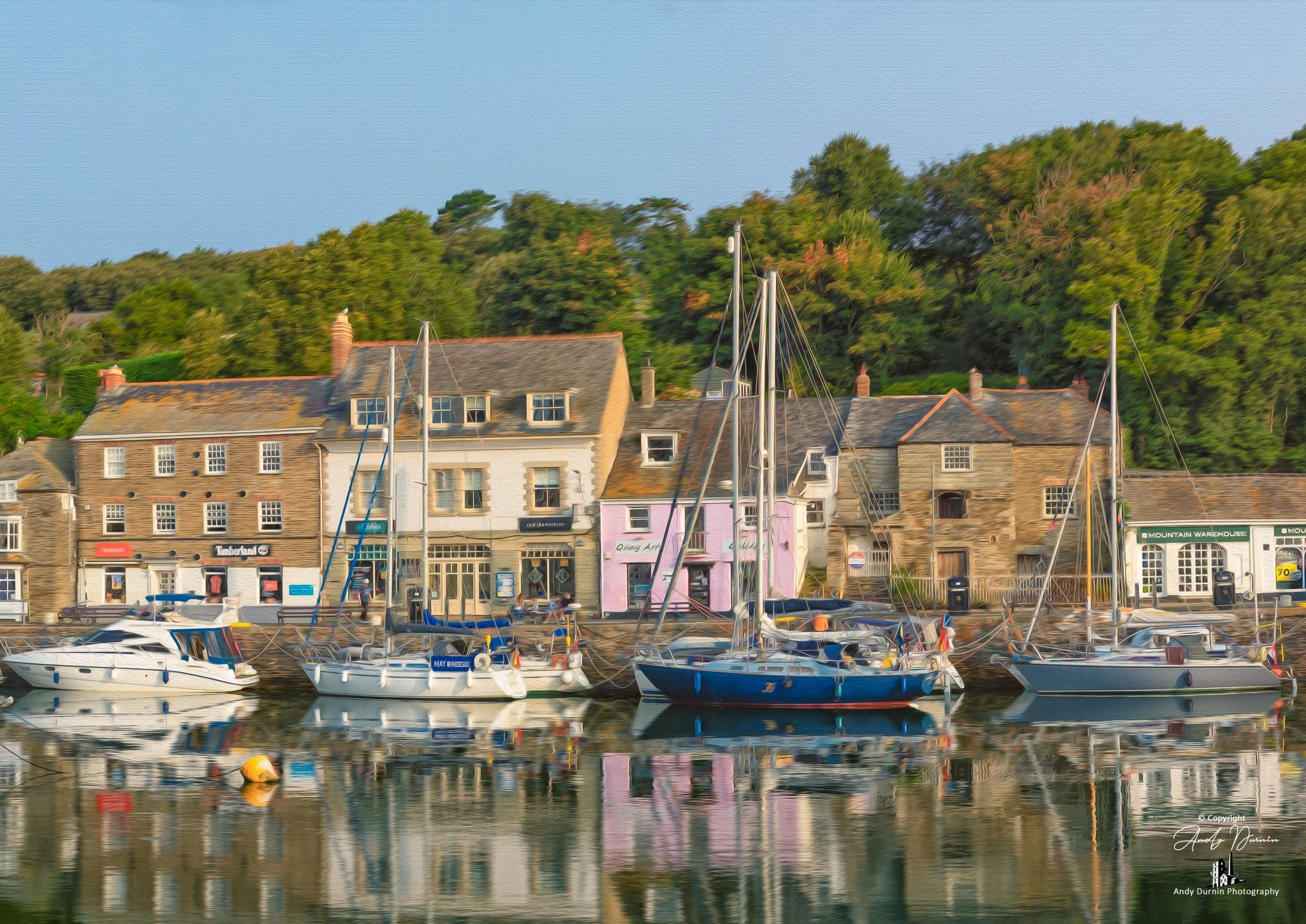 Padstow Harbour.  Boats moored in a harbour with colourful buildings and green trees in the background.