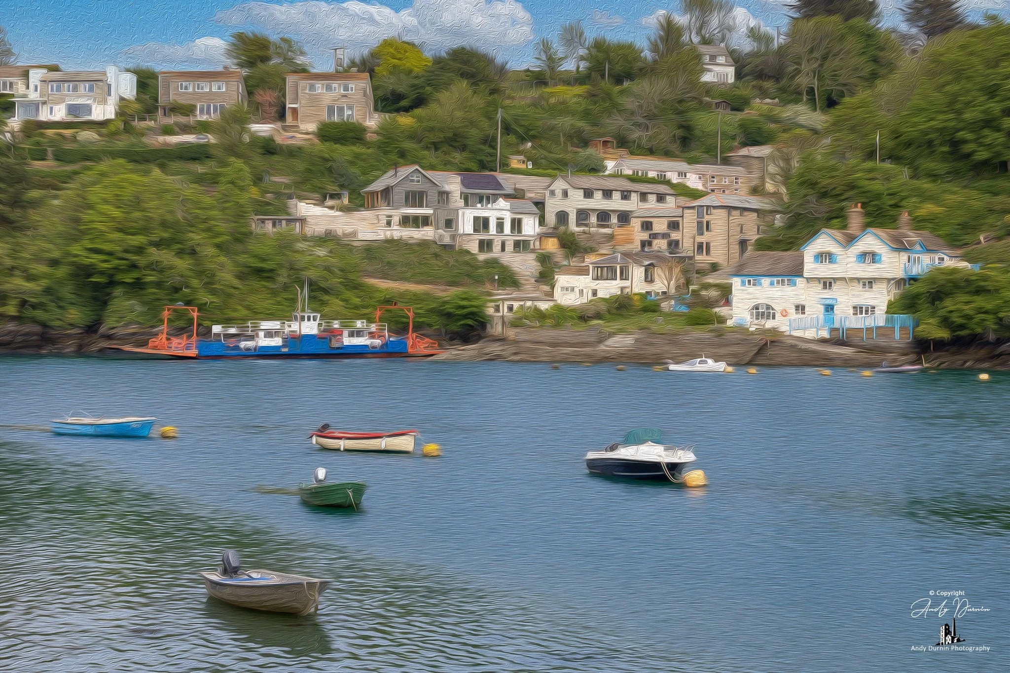 The Bodinnick Ferry on the River Fowey A coastal scene with several boats floating in calm waters near a hillside with colourful houses and greenery.