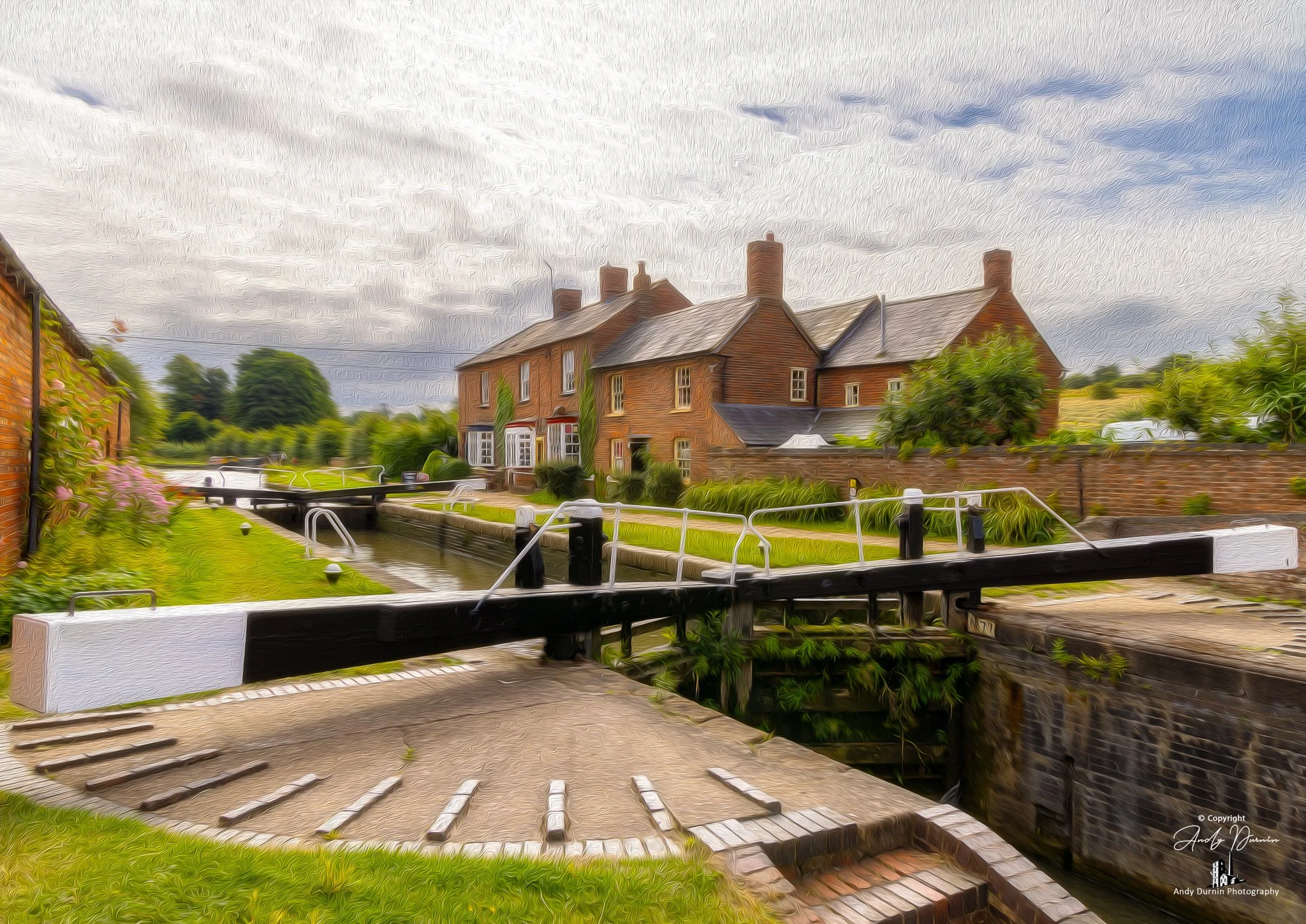 Braunstone Locks.  A picturesque scene of a canal lock with old brick buildings and greenery surrounding it, under a cloudy sky.