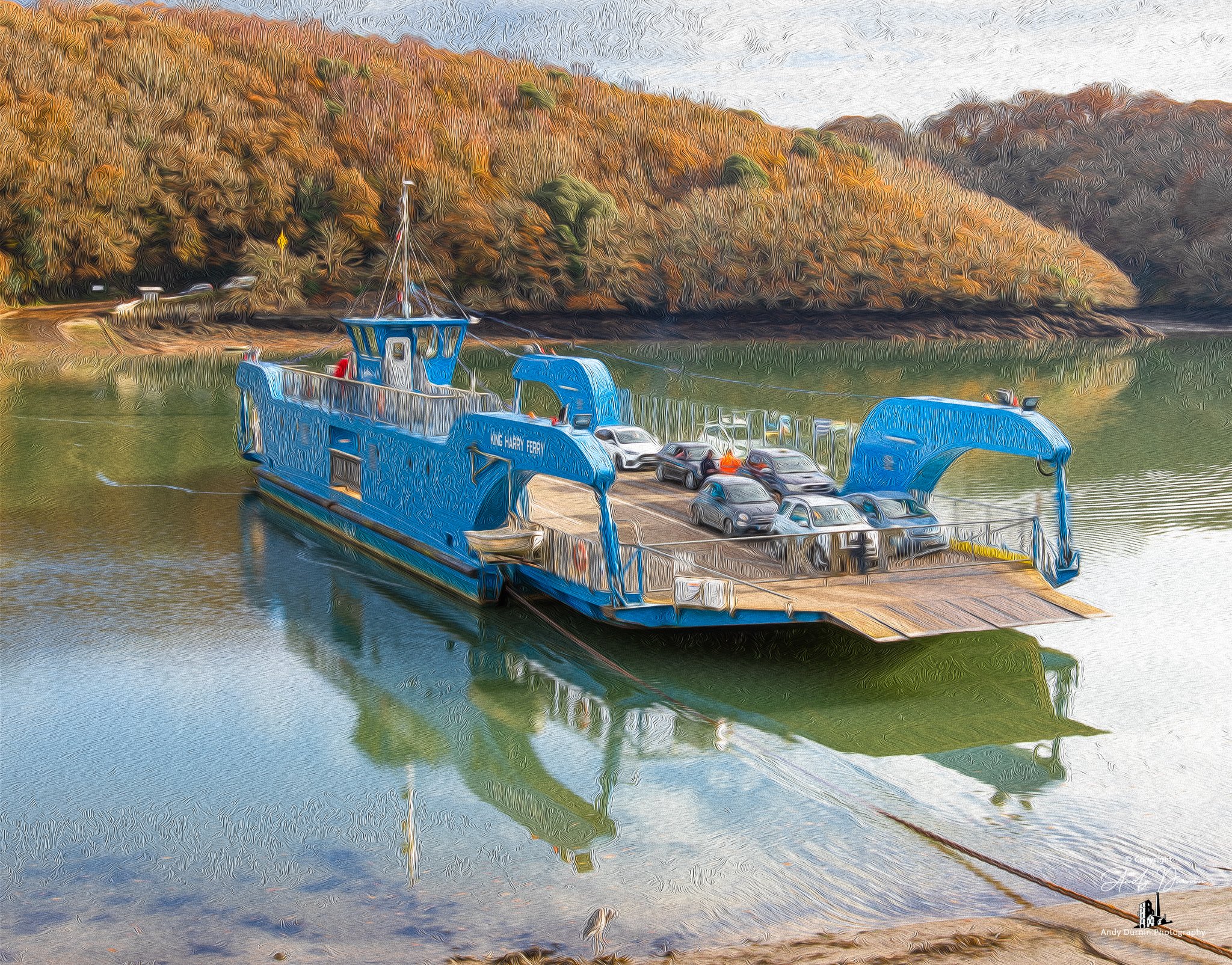A blue ferry boat named King's Ferry over a river, with cars parked on its open deck, surrounded by trees with autumn foliage.