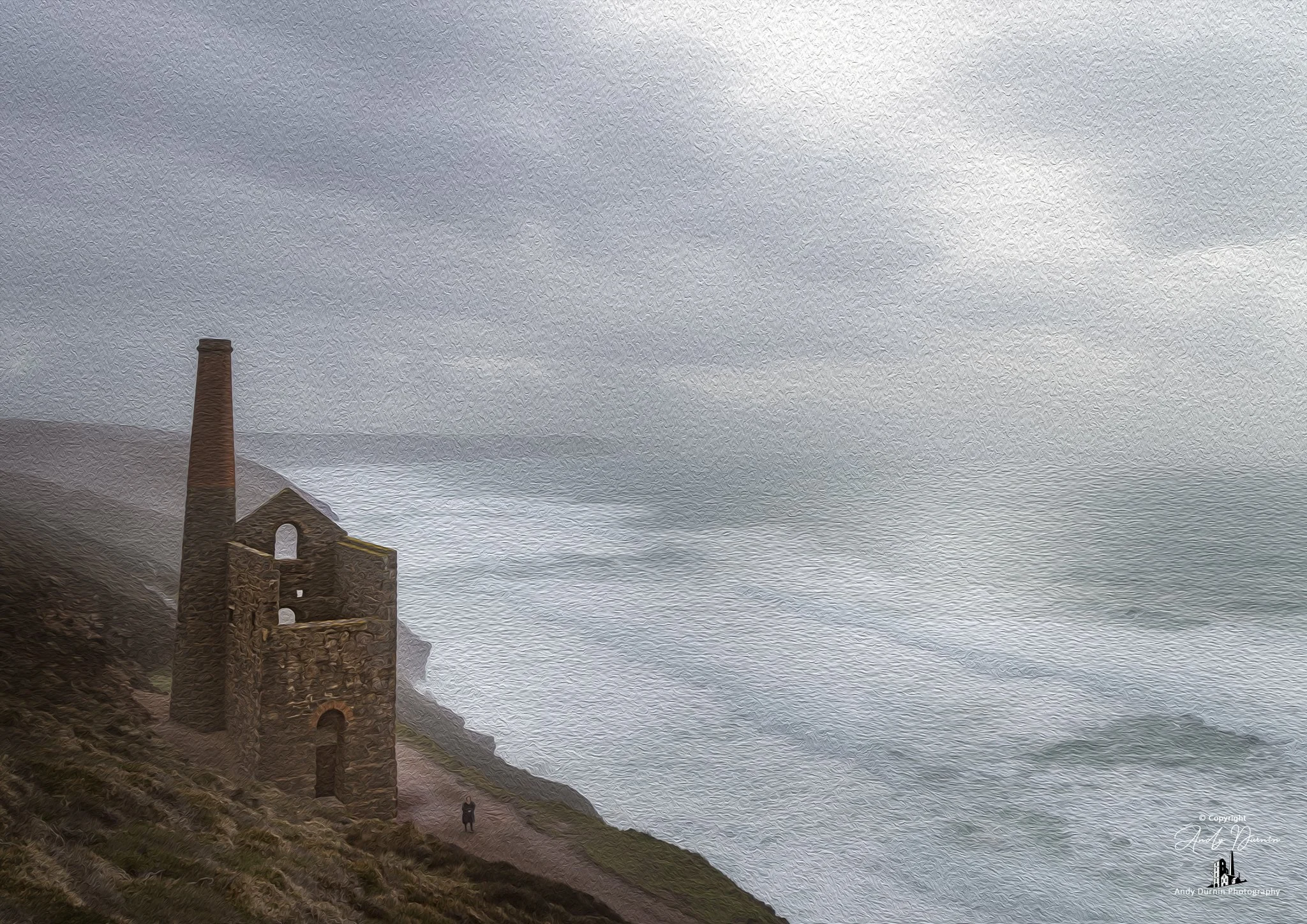 Towanroath at Wheal Coates St Agnes Cornwall abandoned stone building with a tall chimney on a cliff overlooking the ocean with waves. Overcast skies. One person walking near the building.