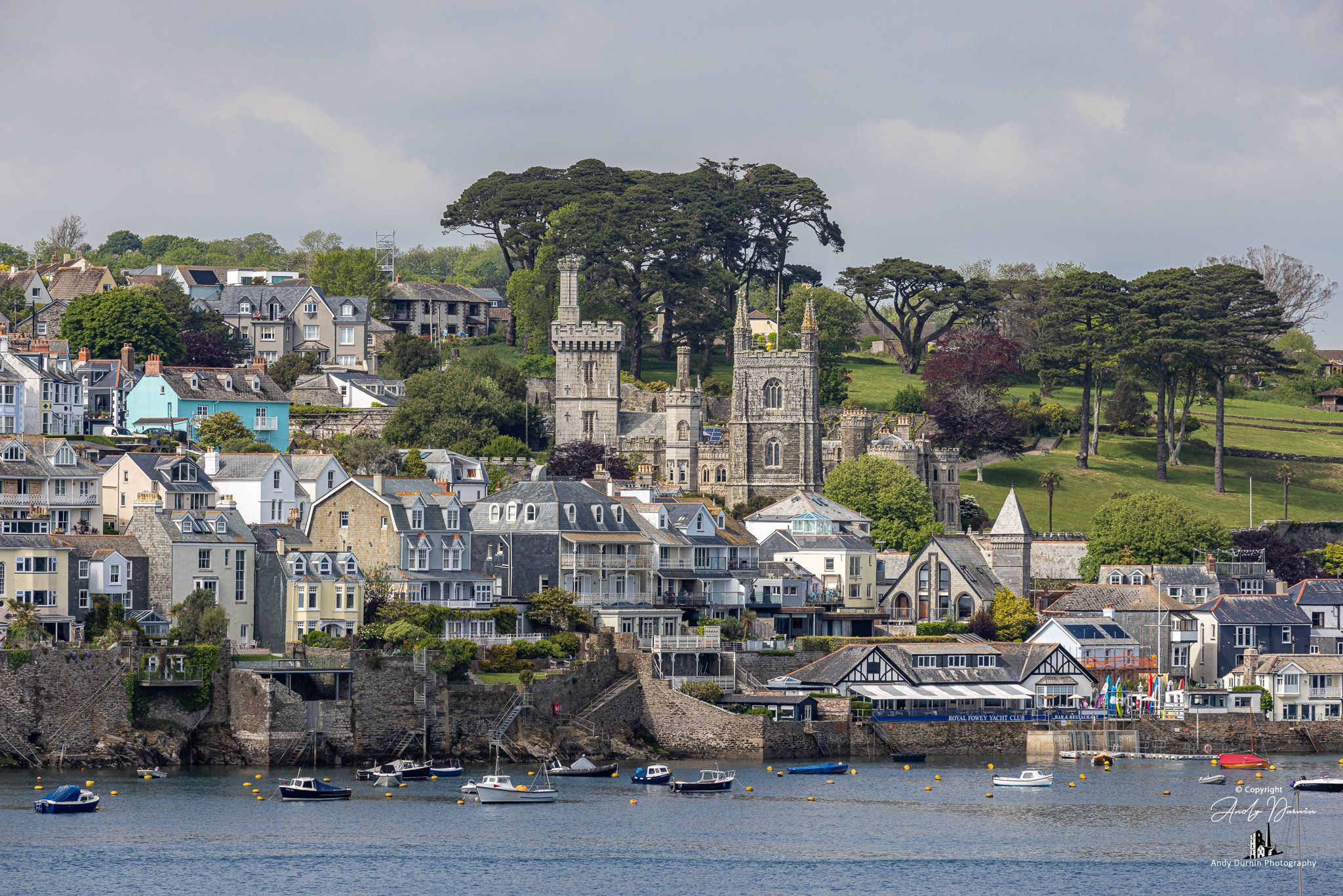 A crisp architectural view of Fowey’s waterfront with the Church of St Fimbarrus and Place House behind, captured across the River Fowey—Cornwall fine art print full of character and detail.
