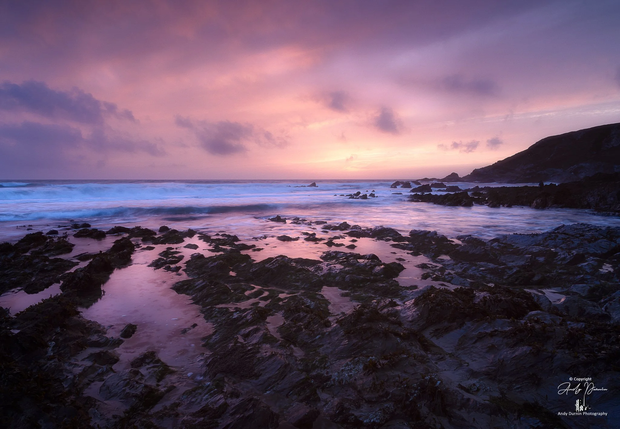 This Dollar Cove sunset print captures a rare and atmospheric moment on the Cornwall coast, as Saharan dust in the atmosphere filled the evening sky with glowing pink, peach and violet tones. With dark foreground rocks, soft reflections and a tranqui