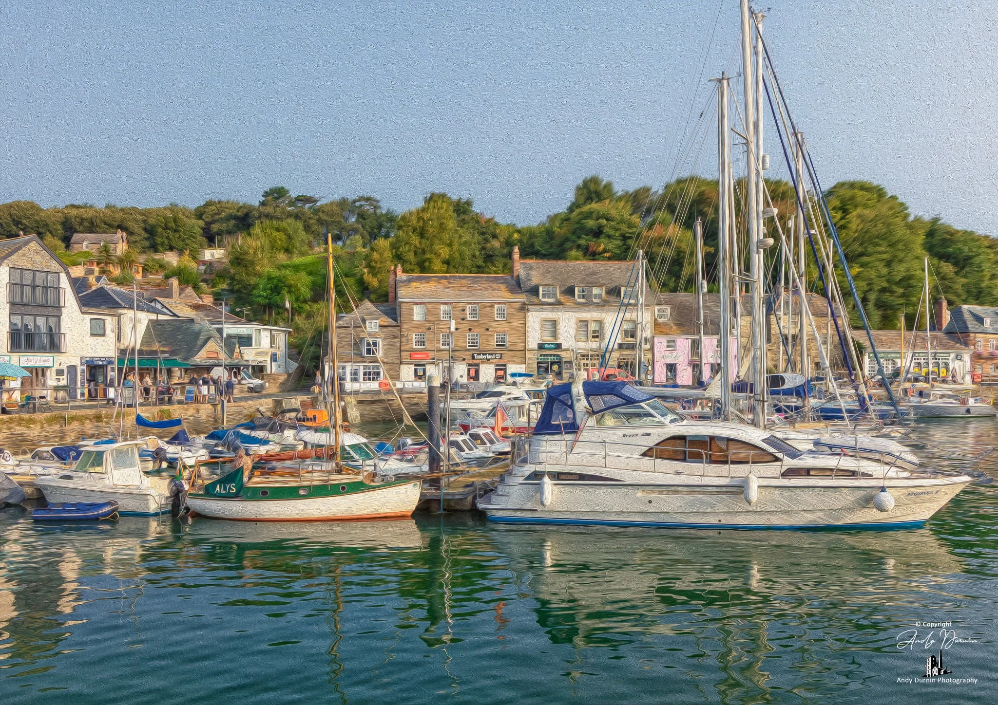 Padstow Harbour.  A harbour with boats moored in water with buildings and trees on the shore in the background.