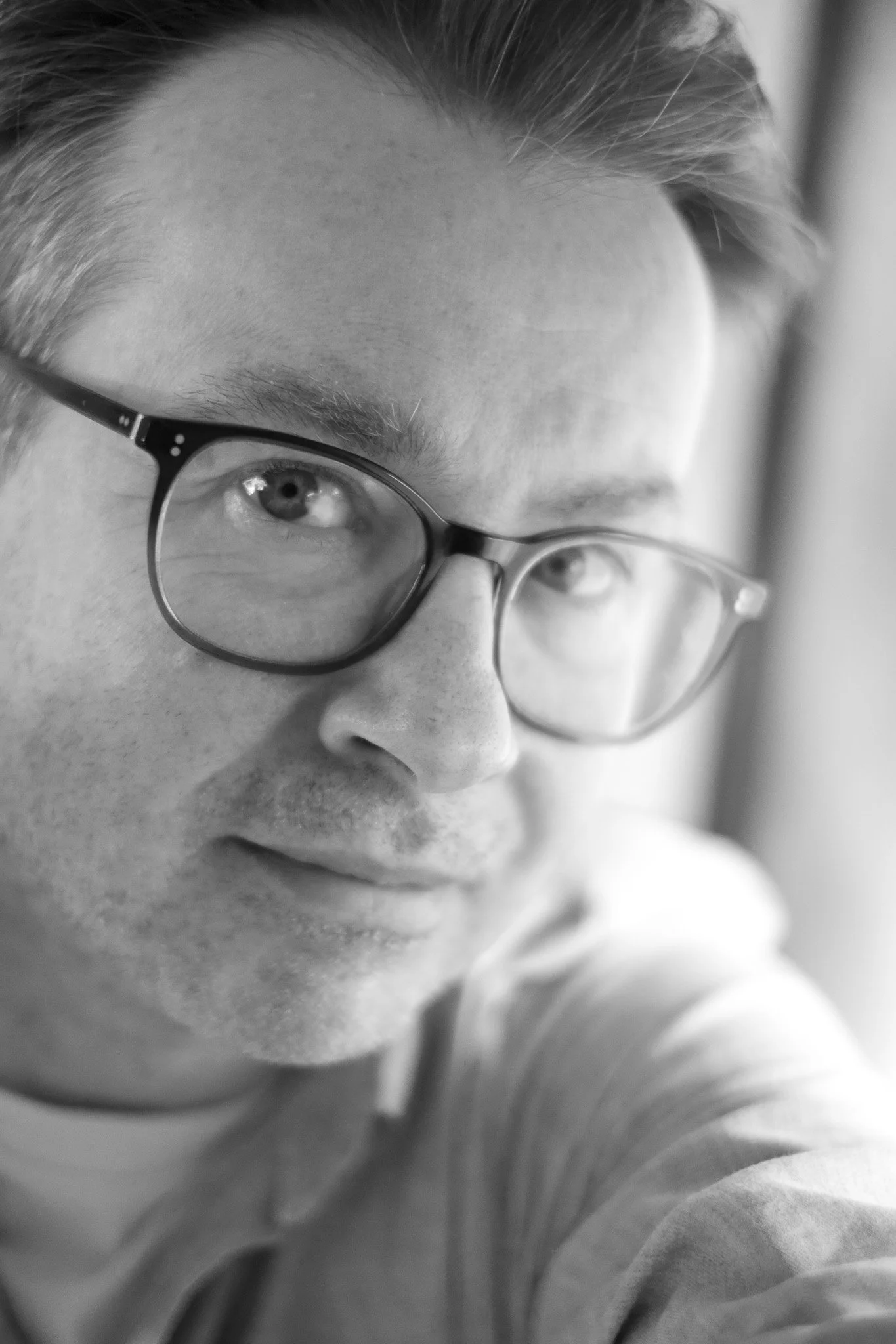 Close-up of a person's face wearing glasses, with short hair, captured in black and white.