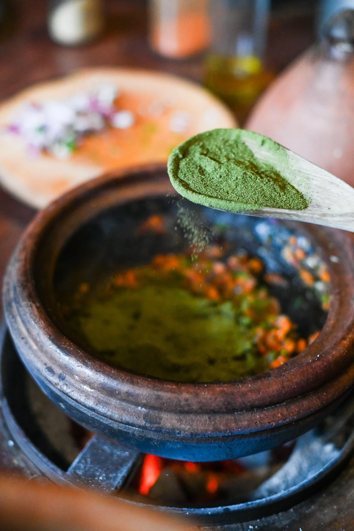 An assortment of “invisible green” dried and ground into a nutrient rich powder, being adding into a clay pot on the stove.