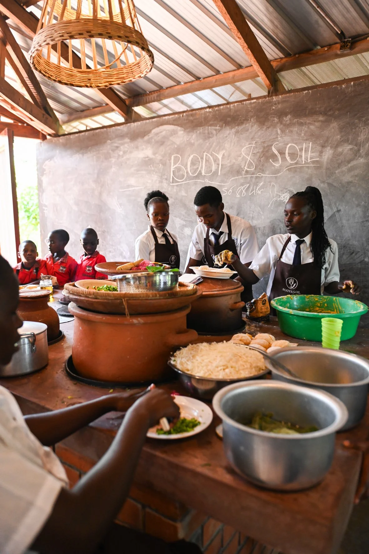 Children in Uganda preparing different food in clay pots in a classroom.