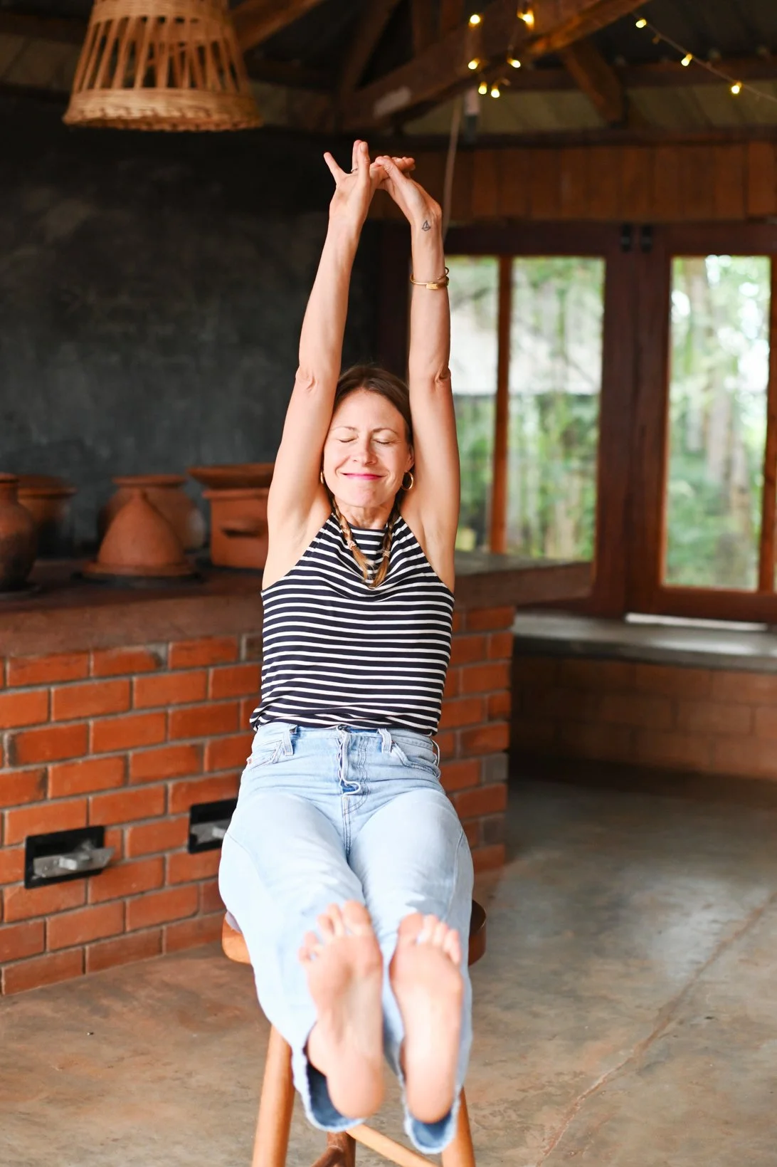 A middel aged woman streching her arms up and smiling a kitchen behind her.