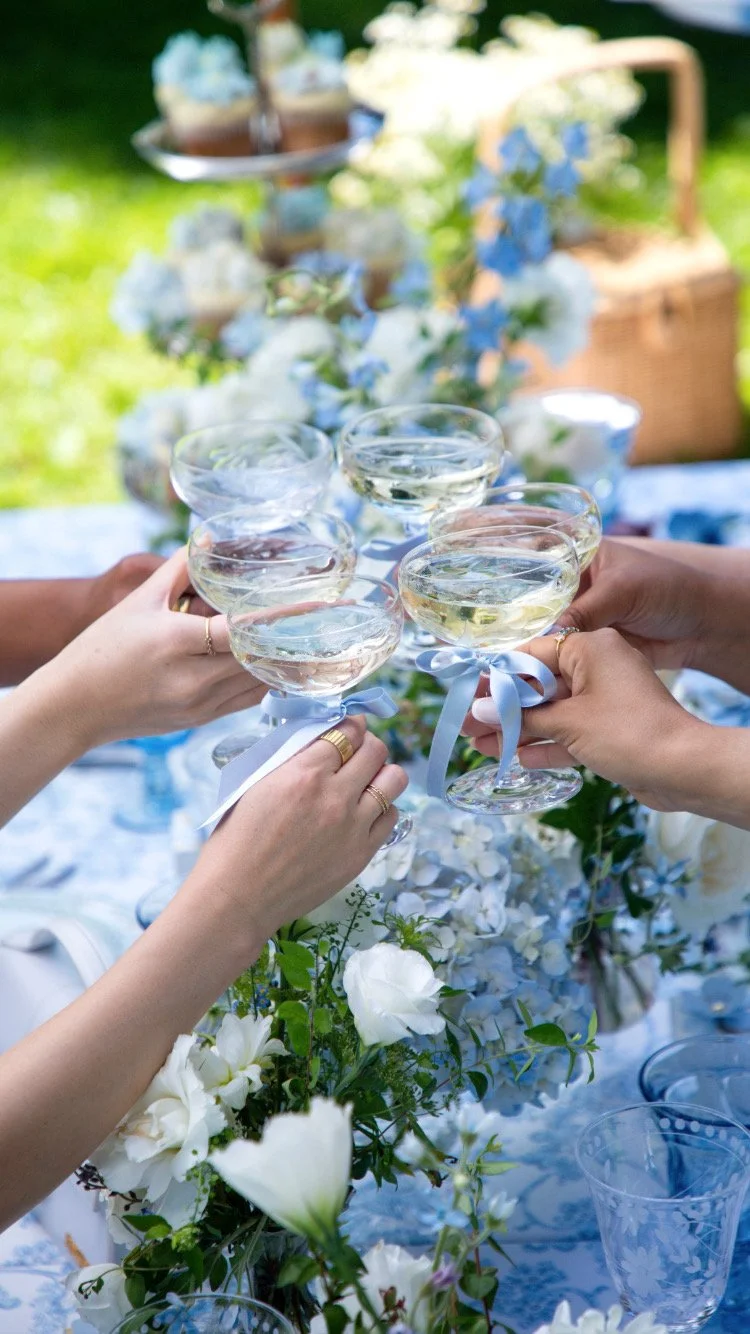 People celebrating with champagne glasses at an outdoor gathering with a floral centerpiece in the background.
