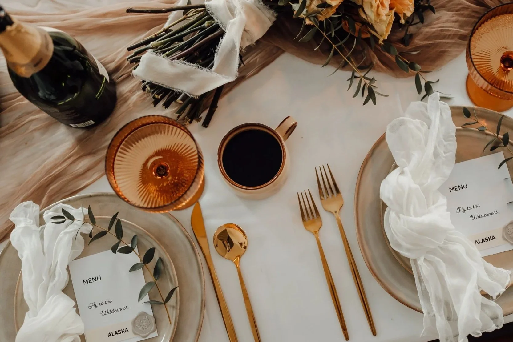 Close-up flat lay of Alaska elopement table details, including menu, linen napkin, glassware, and gold utensils.