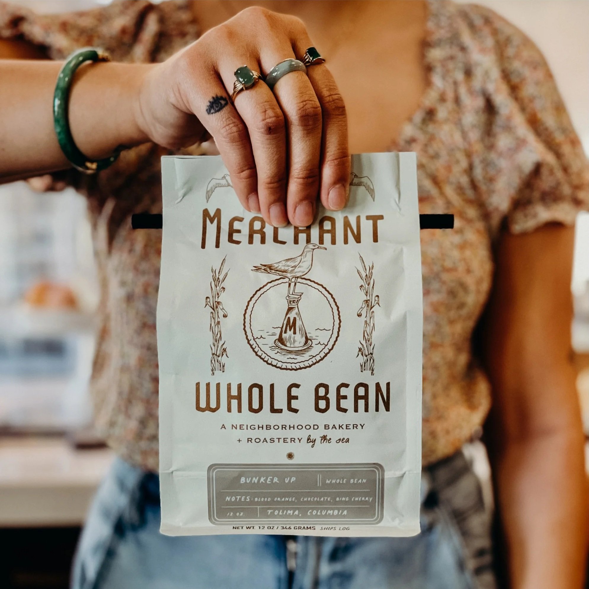 Hand holding a bag of The Merchant whole bean coffee
