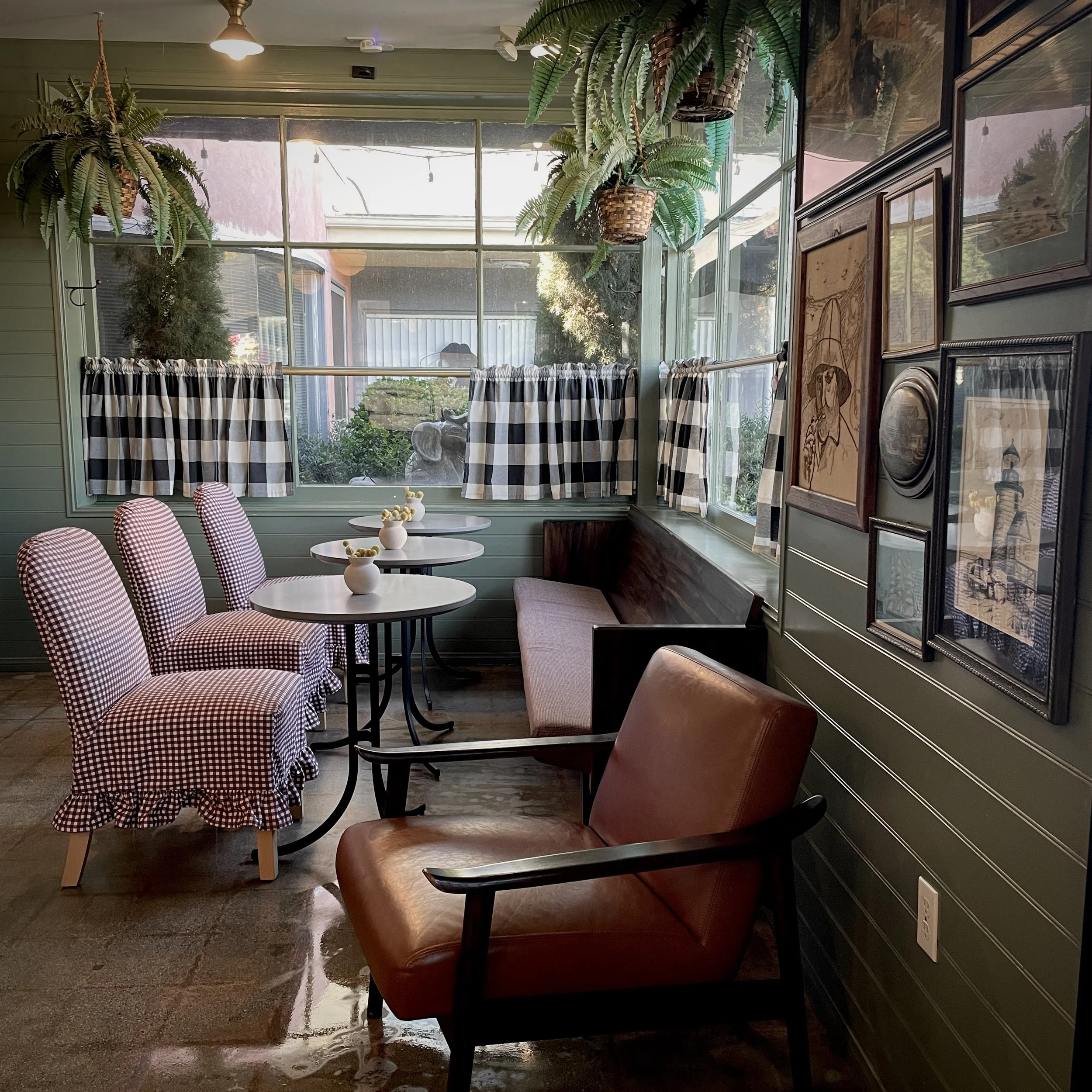 Cozy café nook with gingham chairs, round tables, a leather armchair, and hanging ferns