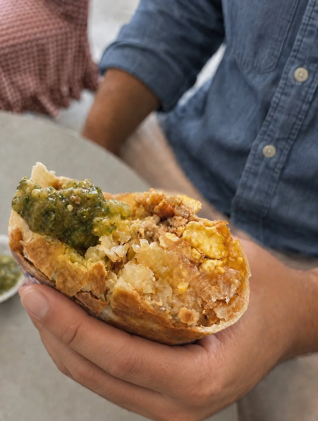 Person holding a breakfast burrito topped with green salsa