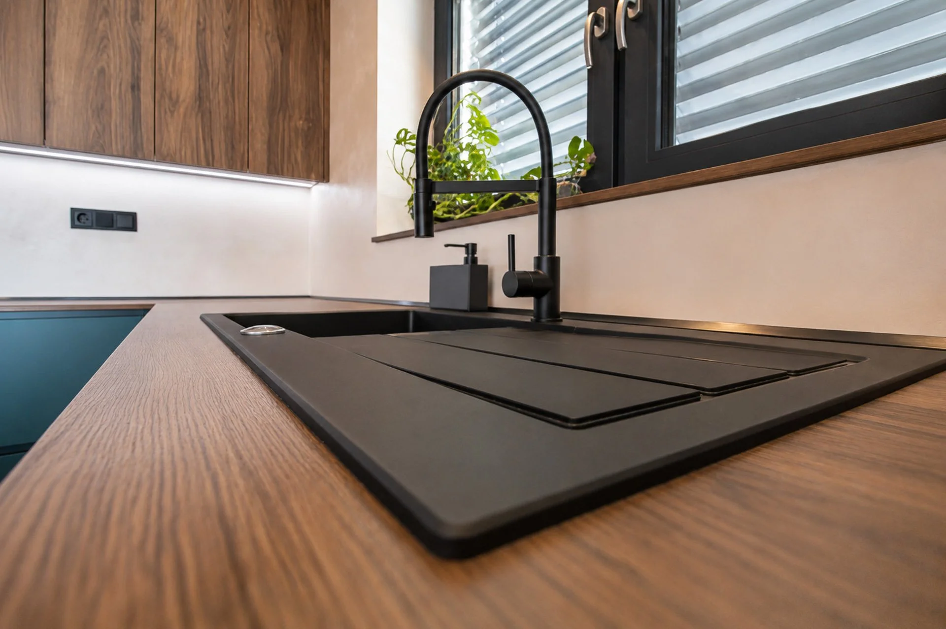 Černý dřez v dřevěné pracovní desce pod oknem a černá baterie (penthouse Šrámkovka, České Budějovice)