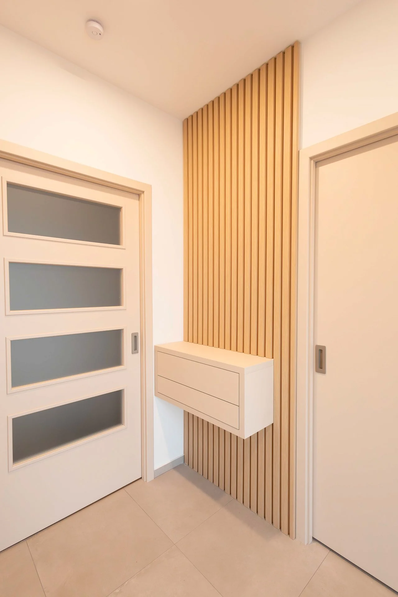 Předsíň s lamelovým dubovým nástěnným obkladem a závěsnou béžovou skříňkou se šuplíky - RD Hluboká nad Vltavou