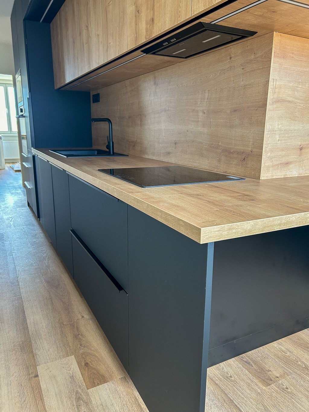 Detail kuchyňské linky s černými úchytkami a pracovní deskou
