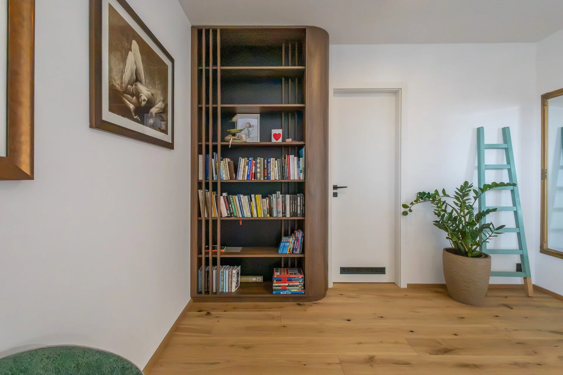 Otevřená knihovna se zaobleným rohem a svislými lištami před tmavým pozadím (penthouse Šrámkovka, České Budějovice)