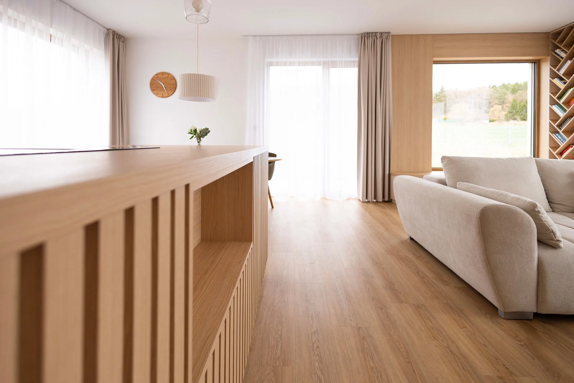 Kuchyně s ostrůvkem s lamelovým frontem, závěsnými svítidly a navazujícím jídelním prostorem - RD Hluboká nad Vltavou