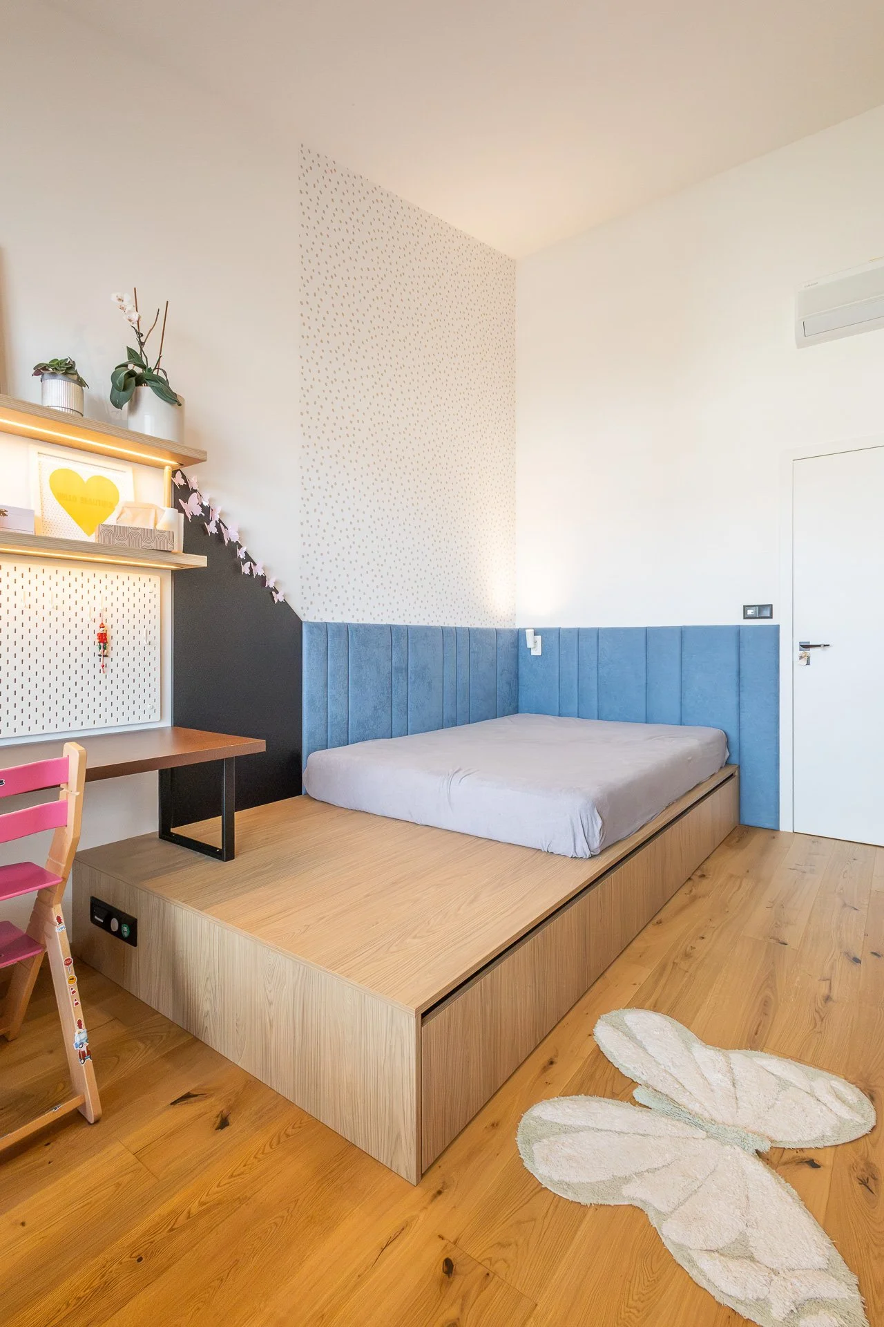 Dívčí pokoj s postelí na dubovém pódiu, modrými panely a navazujícím psacím stolem (penthouse Šrámkovka, České Budějovice)