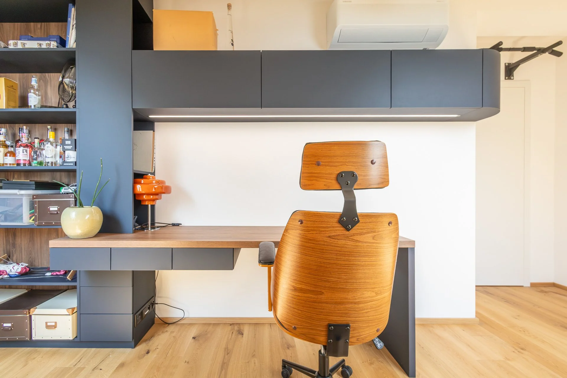 Indigo modrá pracovna s dlouhou dřevěnou deskou a zaoblenými skříňkami s LED (penthouse Šrámkovka, České Budějovice)