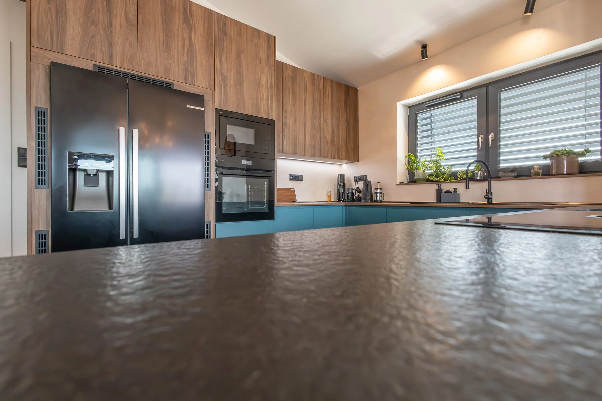 Detail hrubé struktury tmavé kamenné desky ostrůvku a vysokých skříní se spotřebiči (penthouse Šrámkovka, České Budějovice)
