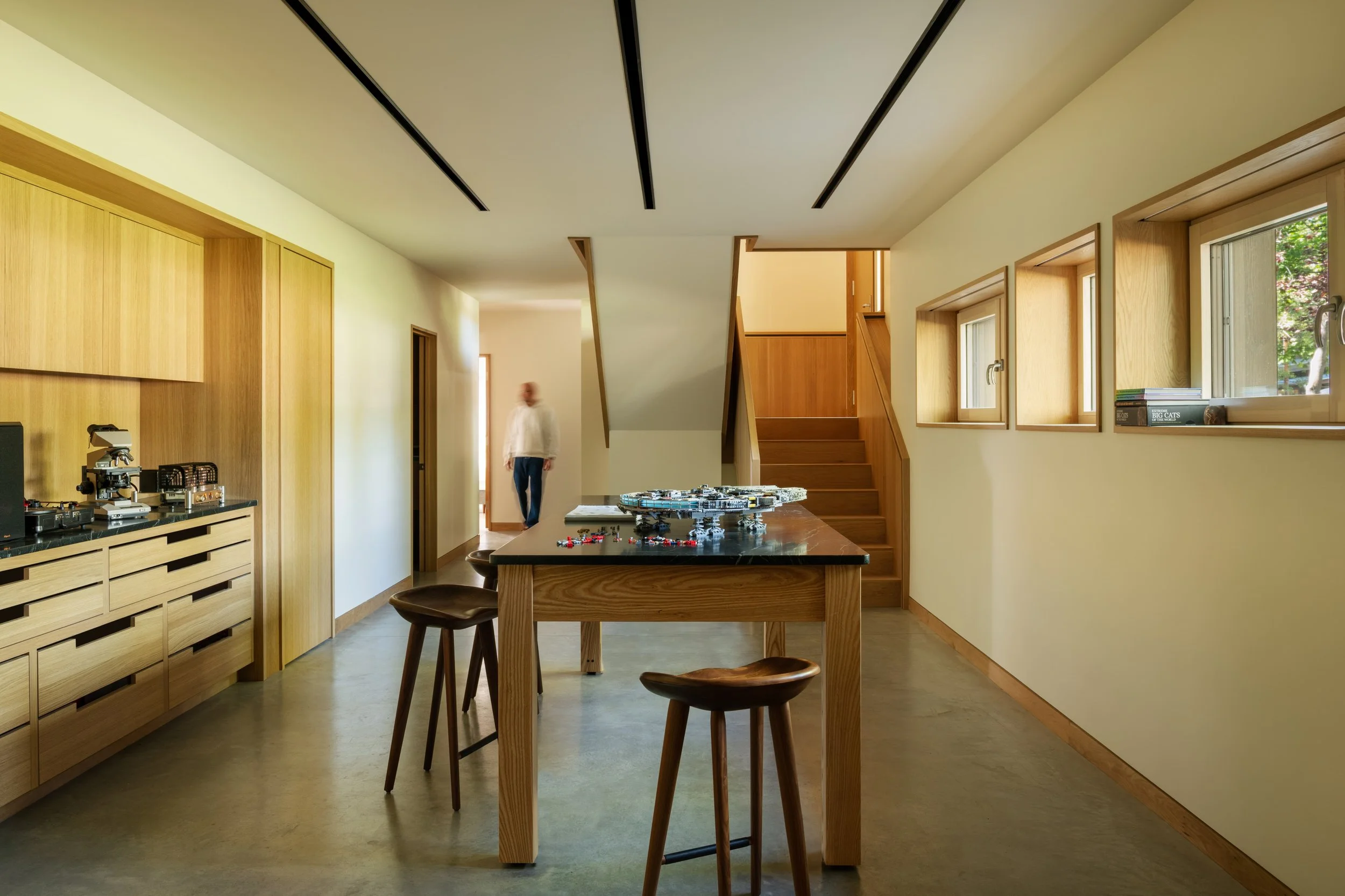 Interior of a modern home with wooden accents, a table with a USS Enterprise LEGO model, and a person walking in the background.