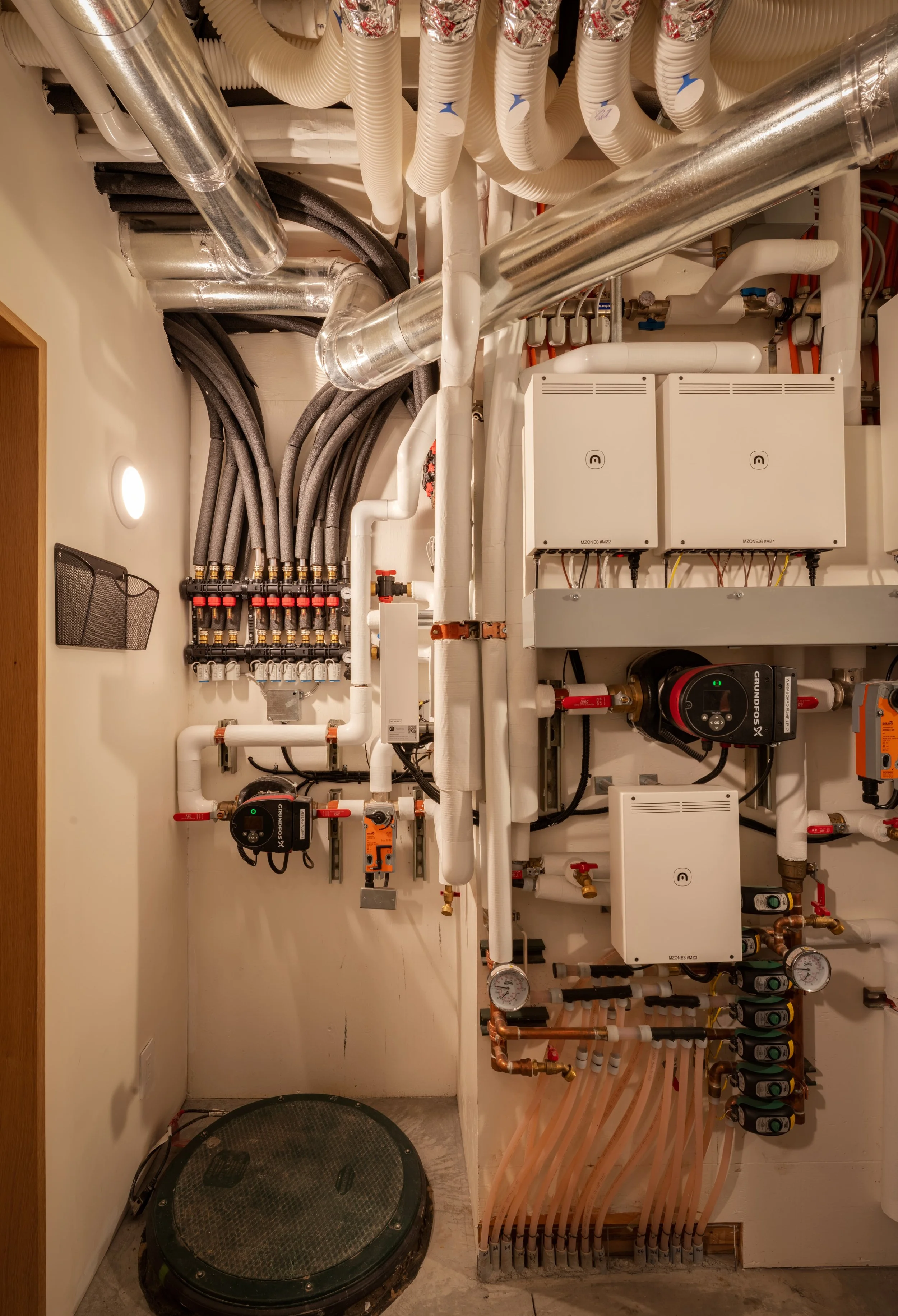 Heating and plumbing pipes, gauges, and control systems in a utility closet.