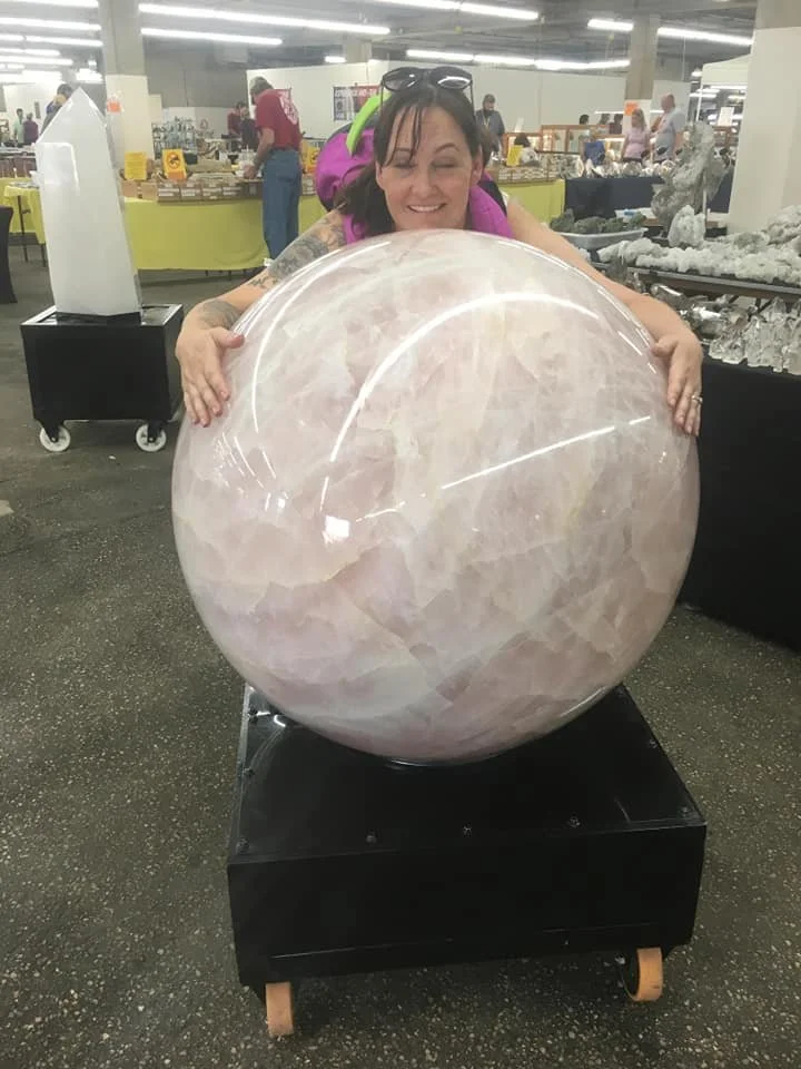 DaNae Sweet at the Denver Gem Show hugging a large rose quartz sphere.