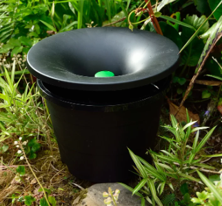 Black compost bin with a green lid in a garden with green plants and grass