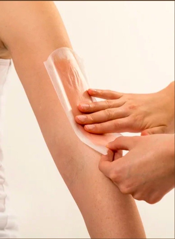 Person applying a waxing strip to an arm, demonstrating hair removal process
