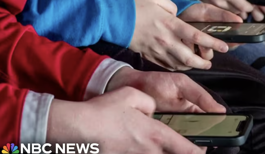 Close-up of people using smartphones, wearing red and blue sleeves. NBC News logo in the corner.