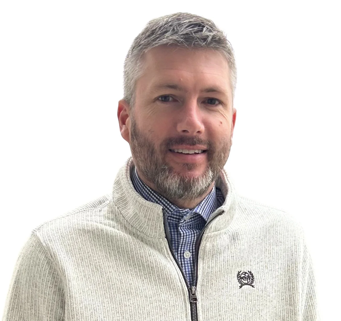 A man with gray hair and beard smiling, wearing a beige zip-up sweater over a blue checkered shirt against a white background.