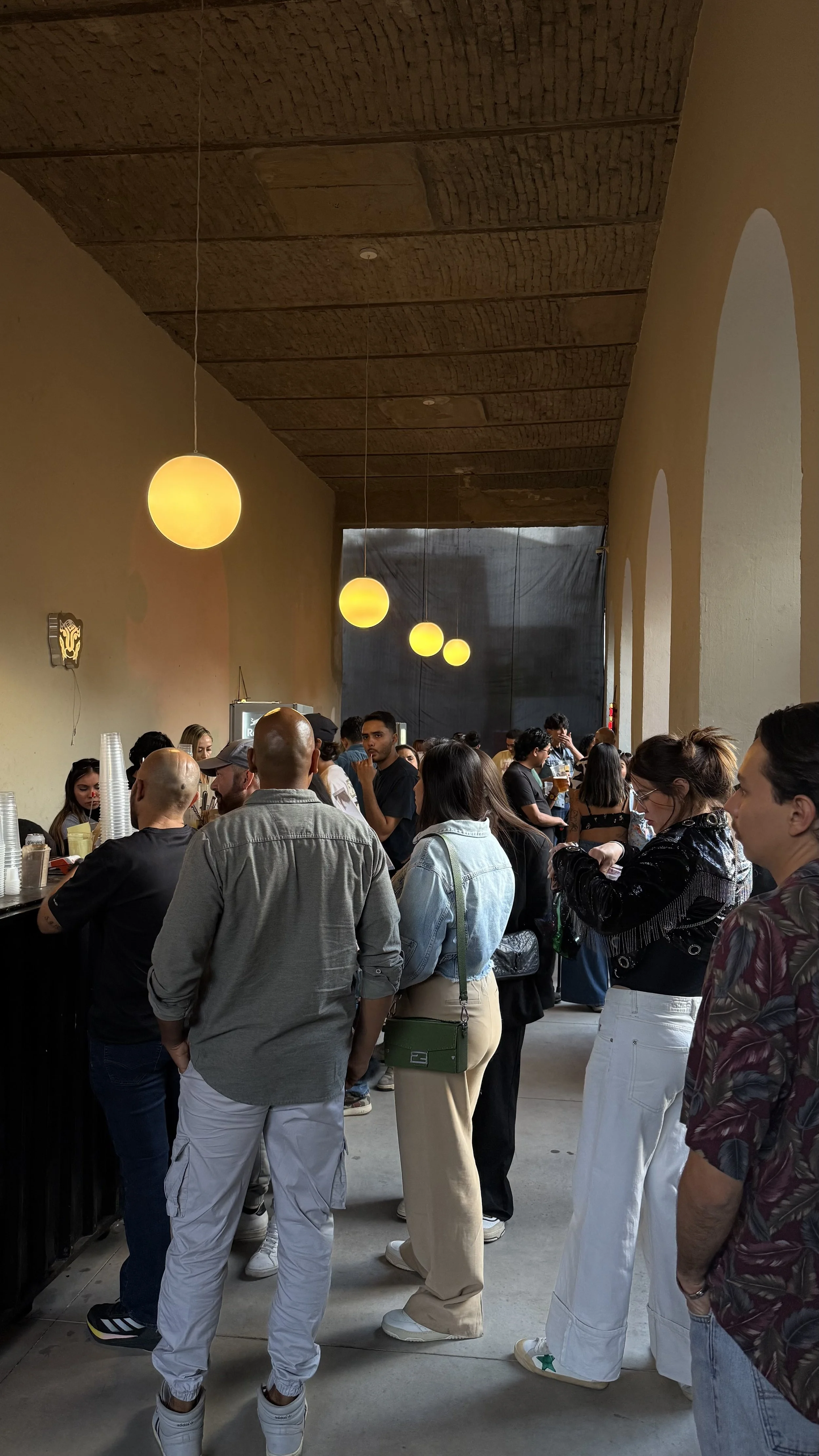 People standing in line inside a cafe or restaurant with hanging yellow lights.
