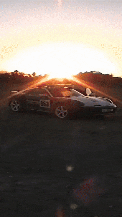 A sleek black sports car with the number 664 on its side, located in a desert landscape during sunset, with the sun setting behind distant mountains.