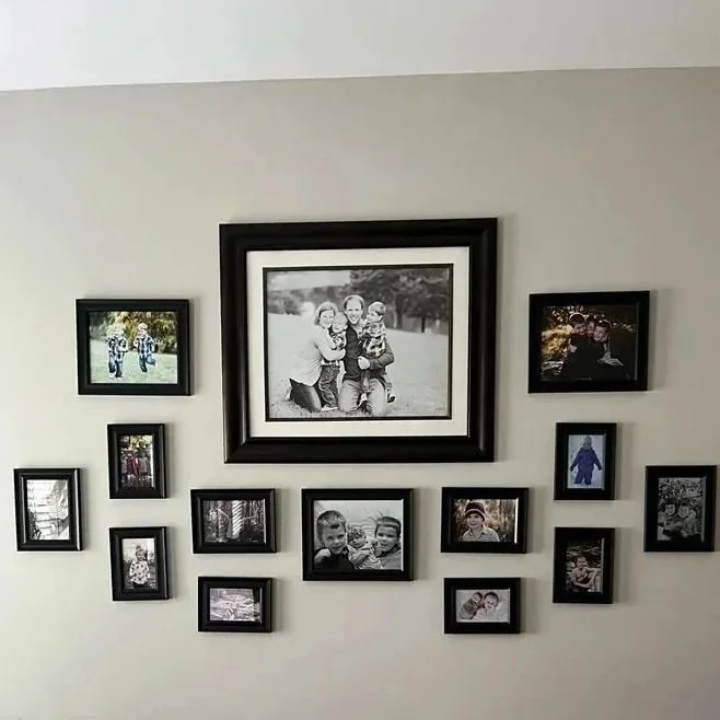 A wall with multiple black picture frames arranged in a collage, featuring family photos of children and adults.