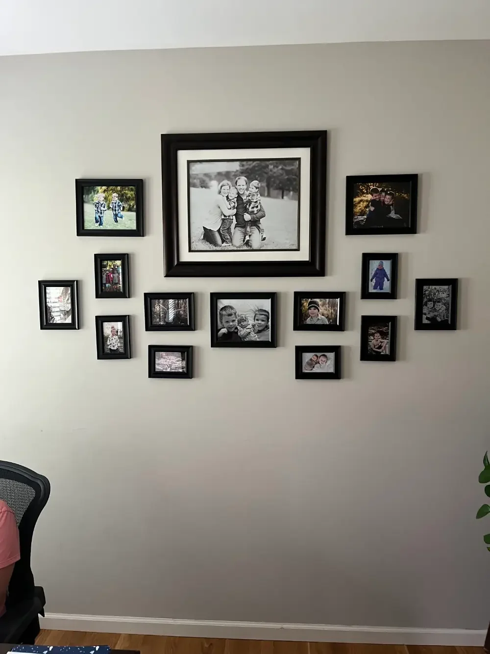A wall decorated with multiple family photo frames, including a large central black-and-white photo of a family with two children, surrounded by smaller color and black-and-white photos of children and families.